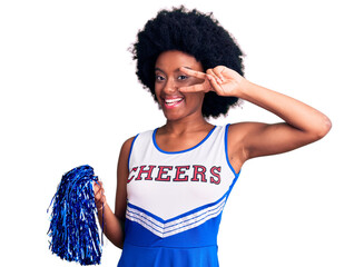 Young african american woman wearing cheerleader uniform holding pompom doing peace symbol with fingers over face, smiling cheerful showing victory