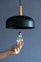 Close-up. A hand changes a light bulb in a stylish loft lamp. Spiral filament lamp. Modern interior decor.