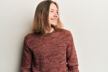 Wall Mural - Handsome caucasian man with long hair wearing casual winter sweater looking to side, relax profile pose with natural face and confident smile.