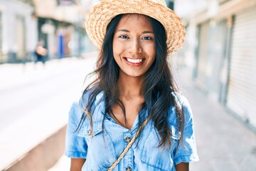 Young beautiful indian woman wearing summer hat smiling happy walking at the city.