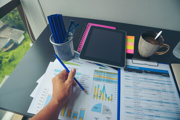 Woman working at home office desk using laptop business financial document chart and graph on wooden table with coffee cup. Woman freelance reading business graphs sale report on business office desk