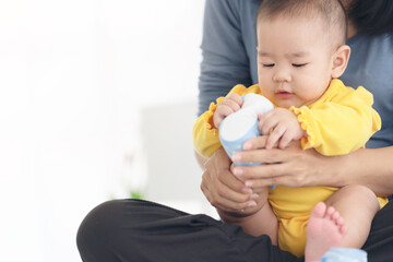 Loving mother putting shoes on baby on sofa at home