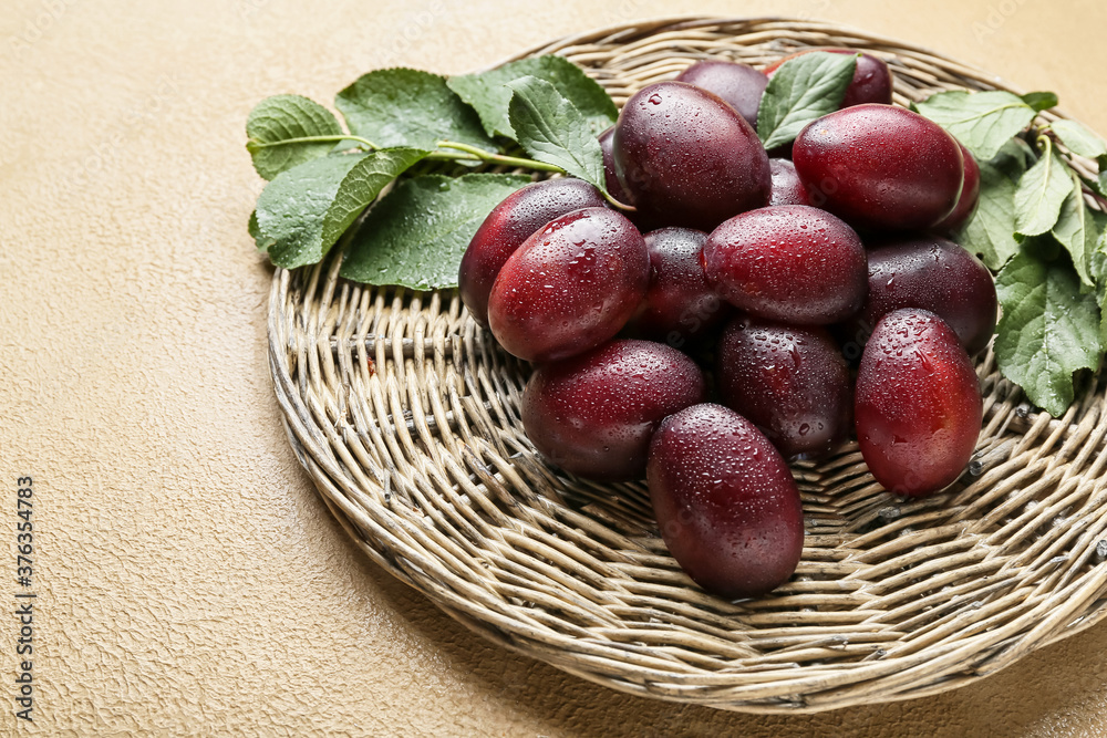 Wicker mat with tasty sweet plums on color background