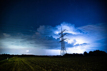 Powerlines In Front Of A Thunderstorm Over A Field