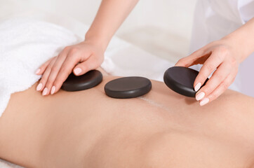 Wall Mural - Spa treatments for beauty. Hands lay hot stones on woman back on massage table