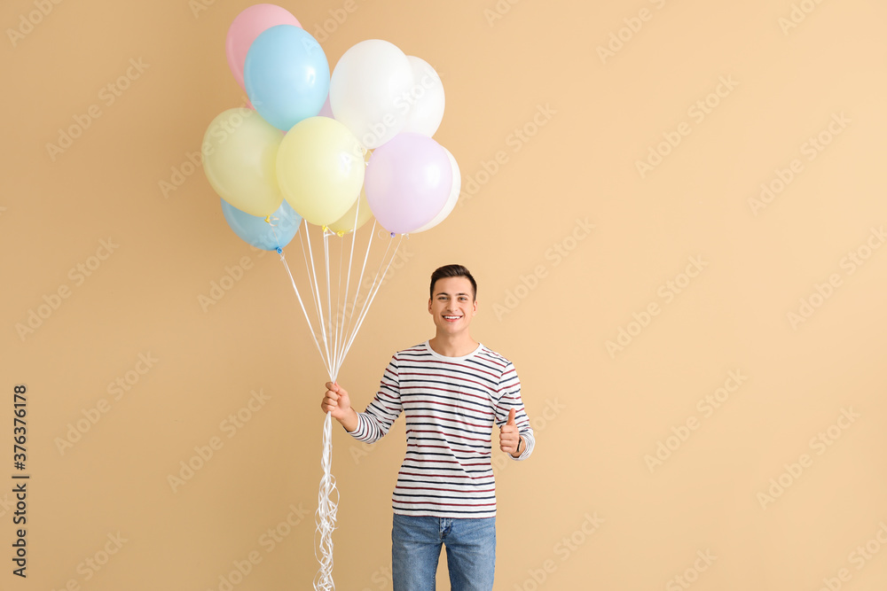 Young man with balloons showing thumb-up on color background
