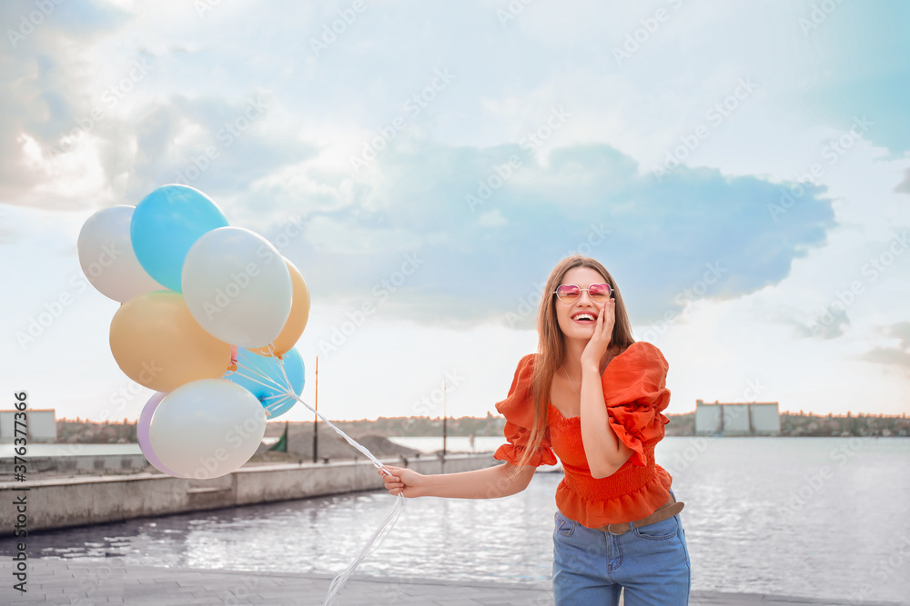 Young woman with balloons outdoors near river