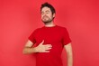 © Roquillo - Young handsome caucasian man wearing t-shirt over isolated red background touches tummy, smiles gently, eating and satisfaction concept.