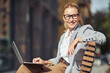 © Kostiantyn - Beautiful succesful middle aged business woman wearing eyeglases sitting on the bench outdoors and working online on laptop