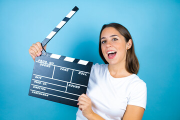 Young beautiful woman over isolated blue background holding clapperboard very happy having fun