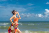 Fototapeta Łazienka - Asian woman wear a colourful bikini stand sunbathing on the sandy beach in a bright day and happy holidays with blue sky 