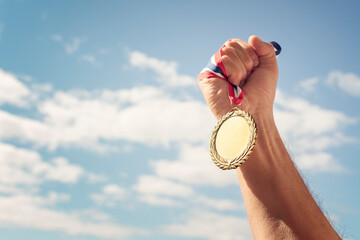 gold medal held in hand raised against sky background