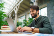 © Halfpoint - Young man with laptop sitting indoors in green office, working.