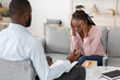 Individual psychotherapy. Depressed black woman sitting on couch at counselor's office