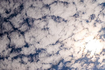 Wall Mural - White clouds pattern in blue sky. The sun shines bright through cumulus clouds in summer. Abstract background and texture concept.