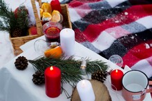 Romantic Picnic In Winter. There Is Mulled Wine On The Table To Warm Up After A Walk. Oranges Were Added To A Cup Of Mulled Wine. There Are Also Candles That Are Redder And Whiter To Create Coziness.
