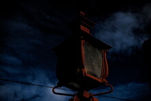 Old Red Lamp Post In The Night, With Dark Gloomy Storm Clouds On The Sky.