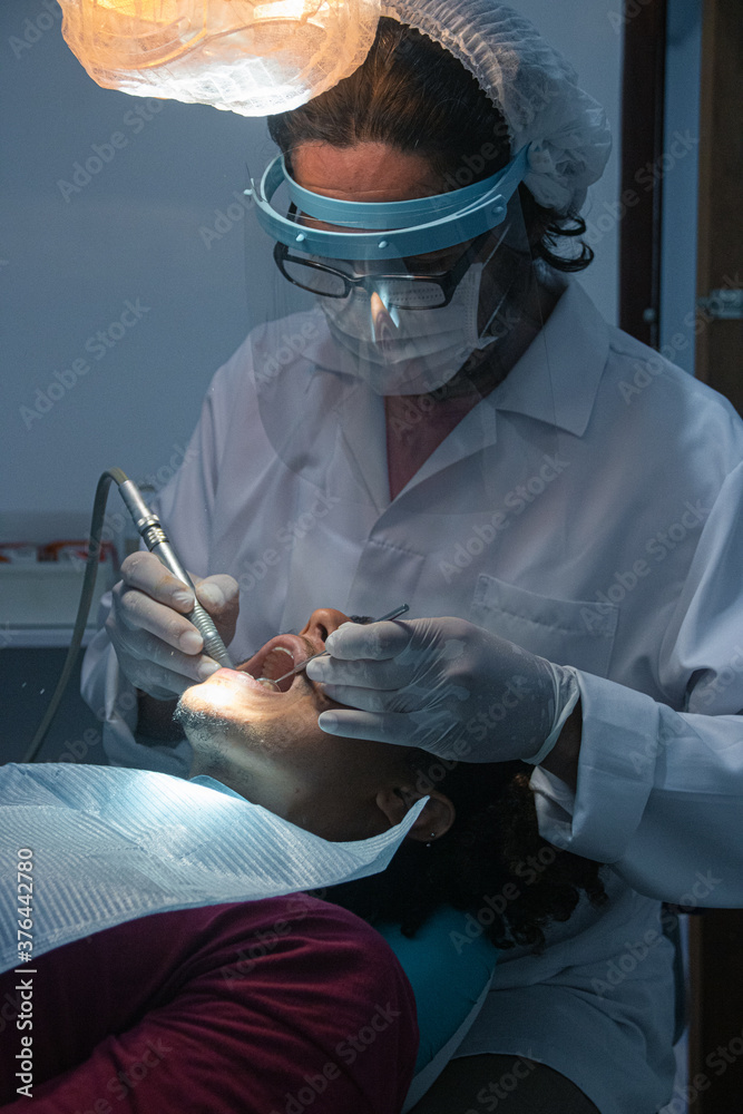 Odontologia avanzada, cuidados confiables. Joven paciente afro-americano en una clinica dentista realizando una limpieza bucal . Dentista examinando los dientes del paciente en una clinica profesional - obrazy, fototapety, plakaty 