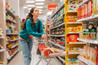 © _KUBE_ - A young beautiful Caucasian woman leaning on a grocery cart, selects products in the store. The concept of shopping and buying products.