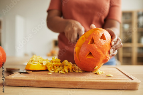 Unrecognizable African American woman standing at table carving Jack-O\'-Lantern out of ripe orange pumpkin