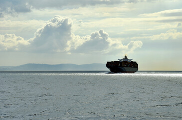 Fully loaded large container ship sailing near African coast on a cloudy day. 