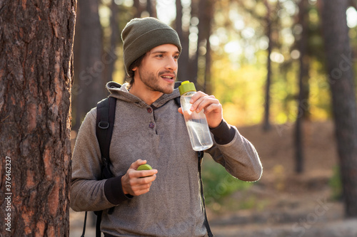 Fotografía Handsome guy drinking water while walking by forest