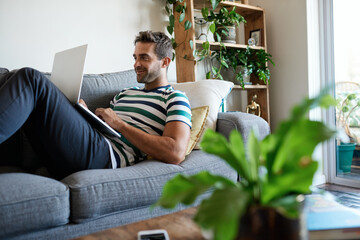 Smiling young man using a laptop on his sofa