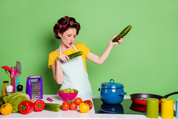 Sticker - Photo of crazy cool girl prepare supper hold cucumber dance have table pepper tomato ingredients wear hair rollers yellow dotted t-shirt isolated over green color background