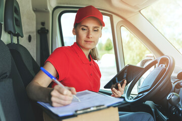 Wall Mural - delivery person in red uniform sitting in van and writing documents on clipboard