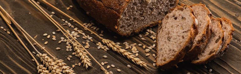 Wall Mural - cut fresh baked bread with spikelets on wooden surface, panoramic shot