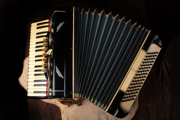 Old accordion on rustic wooden surface with black background and Low key lighting, selective focus.