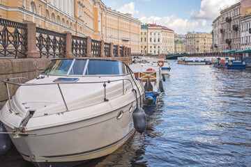 A white boat stands in the city channel against the background of a blurred city.