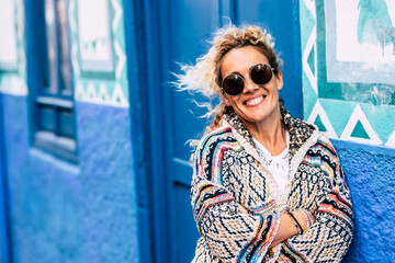 Portrait of trendy beautiful adult woman smile at the camera with blue home wall in background - fashion people with sunglasses enjoy the outdoor leisure activity