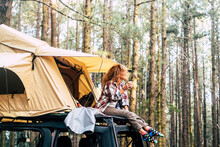 Concept Of Independence, Freedom And Travel With Lonely Woman Sit Down On The Roof Of The Car Outside The Roof Tent - Beautiful Nature And Forest View Outdoor