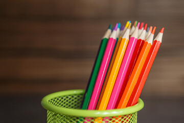 Pens and pencils in metal holder in front of wall background