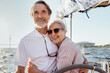 © Artem Varnitsin - Cheerful senior couple standing at steering wheel on a yacht and hugging each other. Happy people enjoying sunny day on a boat.