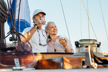 Sticker - Portrait of senior couple standing on a private sailboat and drinking wine. Woman and man with bocals of wine on yacht enjoying trip.