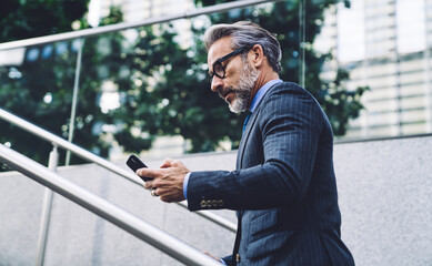 Wall Mural - Serious mature businessman browsing in smartphone in city