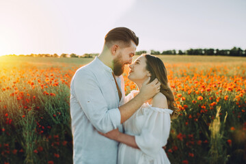 Young beautiful pregnant couple in poppy field. Happy couple walking a poppy field outdoors in summer sunny day.