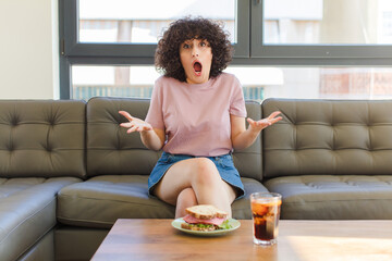 Wall Mural - young pretty arab woman having a sandwich sitting on a sofa at home