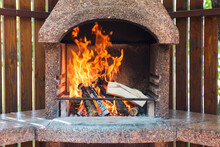 Stationary Barbecue Fireplace With Burning Wood At Summer Day. Outdoor Fireplace And Barbecue