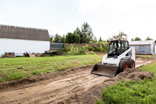 A Skid Steer Loader Clears The Site For Construction. Land Work By The Territory Improvement. Machine For Work In Confined Areas. Small Tractor With A Bucket For Moving Soil And Bulk Materials.