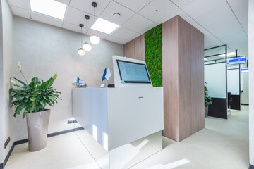 White reception corner with high-tech office equipment. The room decorated with the moss wall and a plant