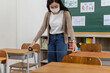 © JR-50 - An Asian teacher uses a tape measure to measure the distance of the student's desk to keep student's social distance in the classroom, preventing the coronavirus outbreak.