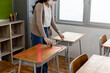 © JR-50 - An Asian teacher uses a tape measure to measure the distance of the student's desk to keep student's social distance in the classroom, preventing the coronavirus outbreak.