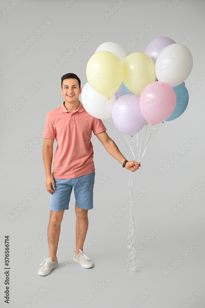 Young man with balloons on grey background