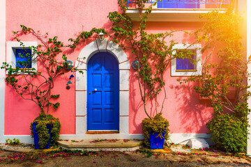  Traditional street with greek houses with flowers in Assos, Kefalonia island. Traditional colorful greek houses in Assos village. Blooming fuchsia plant flowers. Kefalonia island, Greece