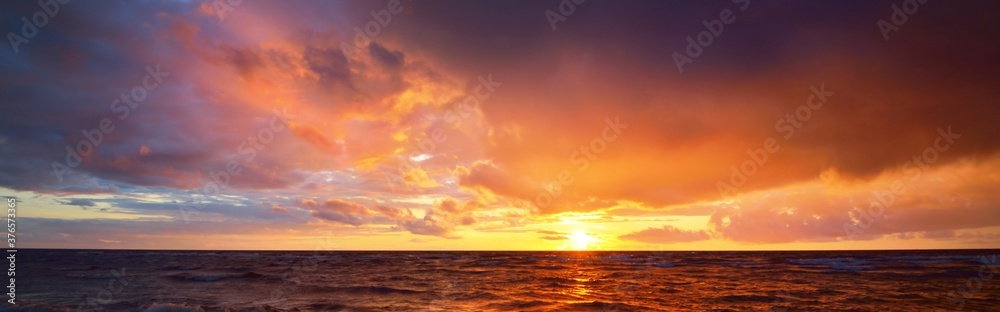 Epic dark sunset sky above the sea shore after the storm. Dramatic glowing colorful red clouds, natural texture, background. Fickle weather, climate change, ecology. Panoramic view - obrazy, fototapety, plakaty 