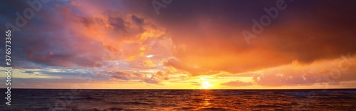 Epic dark sunset sky above the sea shore after the storm. Dramatic glowing colorful red clouds, natural texture, background. Fickle weather, climate change, ecology. Panoramic view