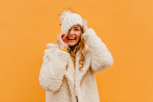 Portrait Of Girl Having Fun On Isolated Background In Woolen Coat. Blonde Puts Hat On Face